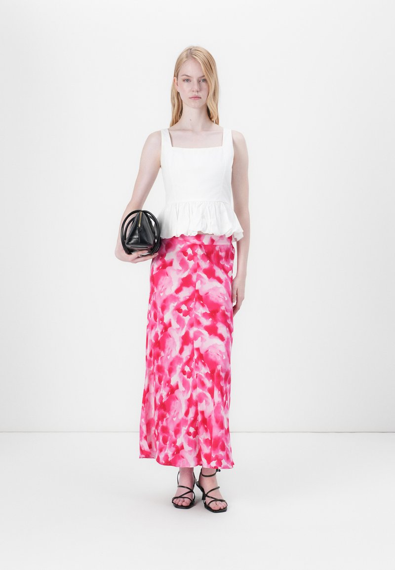 Haut peplum blanc avec décolleté carré, associé à une longue jupe maxi à fleurs roses, tenant un sac à main structuré noir et portant des sandales noires à lanières.