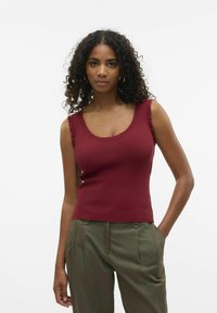 Top de tirantes acanalado burdeos con escote y bordes de hombros con picos, diseño ajustado, combinado con pantalones verdes oliva.