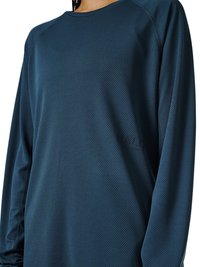 Osoba ubrana w długi rękaw, ciemnoniebieską teksturowaną sportową koszulkę z okrągłym dekoltem, widoczna od ramion do talii.