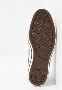 Semelle de basket en toile noire avec caoutchouc brun texturé. Présente un motif géométrique de bande de roulement et un bord blanc, étiqueté "Converse All Star".