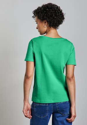 T-shirt en coton vert à manches courtes et col rond, présentant une texture lisse et un ourlet droit, associé à un jean bleu.