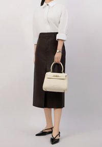 Camicia bianca a bottoni, gonna a matita in pelle nera, ballerine nere con punta a punta e una borsa color crema con un design strutturato e accenti dorati.