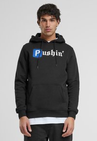 Felpa nera con tasca frontale, caratterizzata dalla scritta in corsivo bianco "Pushin'" e da un riquadro blu che mette in evidenza la lettera "P". Tessuto morbido, con cappuccio regolabile.