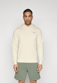 Sweat-shirt beige à capuche avec une poche kangourou et un logo "BORG" brodé. Associé à un short vert olive, le tout en tissu doux.