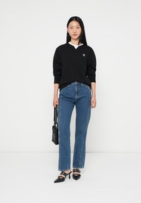Sort sweatshirt med hvid krave, blå højlivede jeans og sorte slingback hæle. Tilbehør med en lille sort håndtaske.