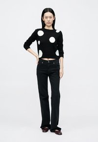 Black cropped sweater with large white polka dots, paired with high-waisted black jeans and burgundy shoes. Smooth texture and fitted design.