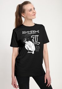 Černé bavlněné tričko s grafickým motivem zobrazujícím kroužící postavu, textové prvky a výrazné logo "L" v bílé barvě.