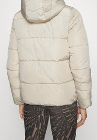 Lys beige pufferjakke med hætte, quiltet tekstur og elastiske manchetter. Skinnende materiale med en cropped pasform, kombineret med mønstrede leggings.