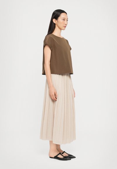 Top court en marron, jupe maxi plissée beige et ballerines noires à bout pointu, mettant en valeur des textures lisses et des lignes de design simples.