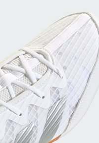 Biele športové tenisky s textúrovaným sieťovaným zvrškom, striebornými akcentmi a cik-cak vzorom na boku. Šnúrky sú biele, so spevnenou špičkou.