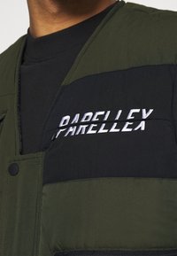 Gepolsterte Weste aus dunkelgrünem und schwarzem Stoff, mit einem weißen, gestickten "PARELLEX"-Logo, Knopfverschluss und strukturierter Oberfläche.