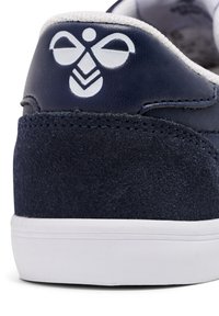 Granatowe sneakersy ze skóry i zamszu z białym logo na pięcie, z białą gumową podeszwą i teksturowanym wierzchem.