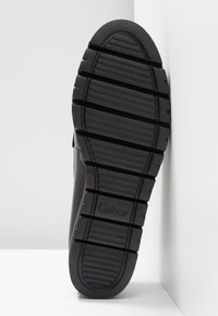 Semelle de chaussure en caoutchouc noir avec de profonds cannelures pour l'adhérence et une finition texturée. Présente un logo en relief dans la zone du talon.