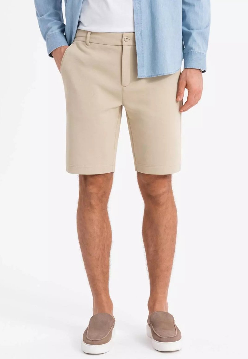 Shorts beige con un design a vita piatta e tasche laterali. Realizzati in tessuto leggero, presentano una chiusura a bottone e sono lunghi fino al ginocchio.