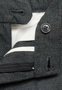 Temno sivo teksturirano blago s vzorcem houndstooth, ki prikazuje črn gumb, belo oblogo in kontrastno horizontalno črto.