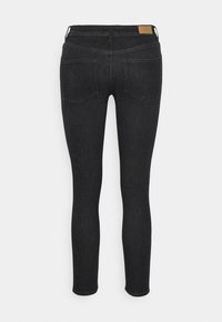 Jean skinny en denim noir avec une texture lisse, présentant deux poches arrière et une étiquette en cuir beige sur la taille.