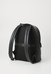 Sac à dos noir avec un extérieur texturé et des bretelles plates, doté d'un matériau en maille à l'arrière et d'une finition lisse sur les côtés.