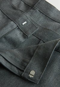 Ceinture de pantalon gris foncé avec fermeture éclair et agrafes métalliques, montrant les coutures détaillées et la texture du tissu.