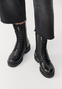 Schwarze Leder-Kampfstiefel mit Schnürung vorne, robustem Sohlen und Reißverschlussdetail an der Seite. Glatte Textur und rundes Zehendesign.