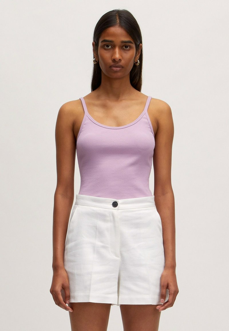 Lichtpaarse geribbelde tanktop met dunne spaghetti-schoenen, gecombineerd met witte linnen shorts met een knoop aan de voorkant en zijzakken.