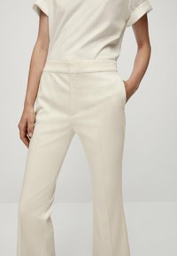 Pantaloni su misura di colore crema con vita alta, gamba dritta e pieghe sottili. Tessuto morbido con tasche laterali.