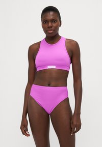 Ροζ δίοσμα μαγιό που περιλαμβάνει crop top με ψηλό λαιμό και ψηλόμεσα μπικίνι. Κατασκευασμένο από απαλό, ελαστικό ύφασμα; εμφανίζεται λογότυπο.