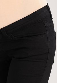 Black denim jeans with a smooth texture, featuring a mid-rise waist, five-pocket design, and subtle stitching details along the seams.