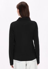 Camiseta de forro polar negro de manga larga con un alto cuello, textura suave y dobladillo curvado, combinada con denim claro. Vista trasera, sin cierres visibles.