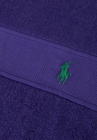 Μωβ υφασμάτινη υφή με οριζόντια ταινία που φέρει μικρό πράσινο κεντητό λογότυπο ενός παίκτη πόλο επάνω σε άλογο.