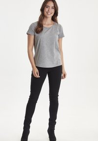 Grå kortærmet t-shirt med rund halsudskæring, parret med sorte slim-fit bukser og sorte ankelstøvler, sat mod en neutral baggrund.