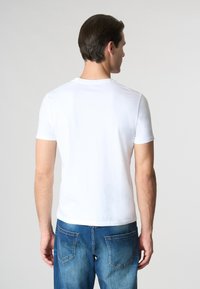 T-shirt bianca a maniche corte realizzata in cotone morbido, con collo rotondo e design aderente; abbinata a jeans in denim blu con tasche posteriori.