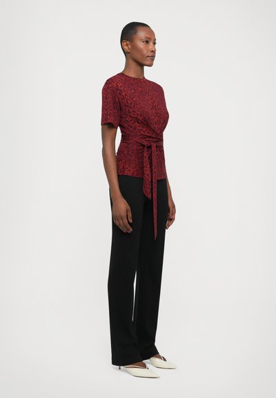 Rood met luipaardpatroon top met een gestrikte taille, gecombineerd met zwarte broek en witte schoenen met een spitse neus. Soepele textuur en aansluitend ontwerp.
