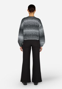 Převelký černý a šedý pletený svetr s texturovaným dip-dye vzorem. Spojen s černými rozšířenými kalhotami. Hladký povrch, volný střih.
