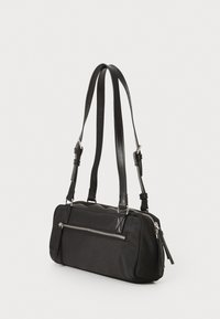 Μαύρη υφασμάτινη τσάντα με ορθογώνιο σχήμα, διαθέτοντας μια μπροστινή τσέπη με φερμουάρ, ρυθμιζόμενα δερμάτινα λουριά και ασημί λεπτομέρειες.