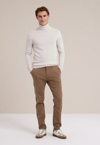 Světlý šedý rolák v kombinaci s béžovými kalhotami a bílými teniskami. Oblečení má slim-fit střih a jemnou texturu.