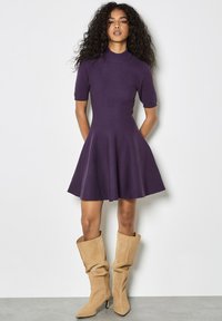 Vestido morado de manga corta con un cuerpo entallado y falda acampanada. Combinado con botas holgadas de color beige, con punta afilada y tacones altos.
