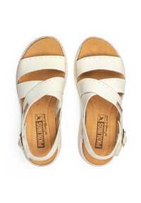 Sandales en cuir gris clair avec des brides croisées, une boucle ajustable et une semelle intérieure texturée couleur tan. Elles présentent un pied de chaussure rembourré et un bord naturel.