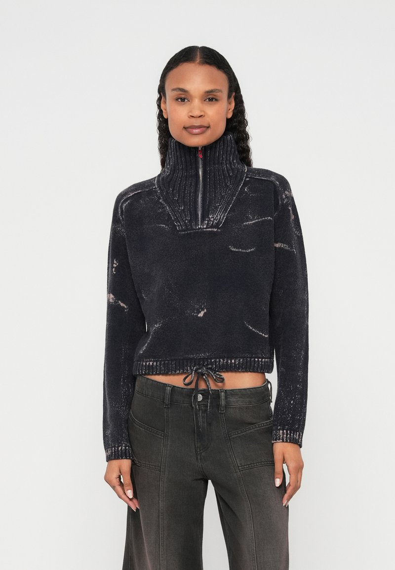 Īsāks, tumši zils džemperis ar augstu apkakli un puszipu, kas izceļas ar teksturētu dizainu. Apakšmalā ir aukliņa ērtākai pielāgošanai.