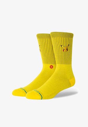 Żółte skarpetki z prążkowanym wzorem i wyszywanym wizerunkiem Pikachu. Zawierają niebieskie i czerwone akcenty na palcach oraz w kostce.