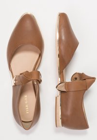 Ruskohvaiset nahkakengät, joissa on terävä kärki, nilkkahihna ja kultainen yksityiskohta korkolapassa. Sujuva rakenne ja minimalismi.