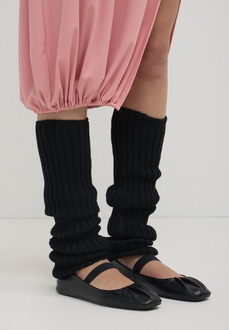 Jambières noires côtelées portées sur les mollets, assorties à des ballerines noires avec un bout arrondi et une bride autour de la cheville.