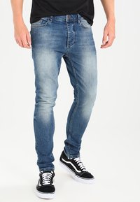 Ljusblå denimjeans med smal passform, med en blekt tvätt, fem fickor och dragkedja. Matcher med svarta och vita sneakers.