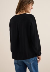 Zwarte blouse met lange mouwen, een gestructureerd gestreept patroon, ronde halslijn en een relaxte pasvorm, ingestopt in blauwe denim jeans.