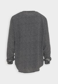 Maglietta a maniche lunghe nera con un motivo a pois bianchi distribuiti, caratterizzata da una vestibilità rilassata, scollo a girocollo e polsini arricciati.