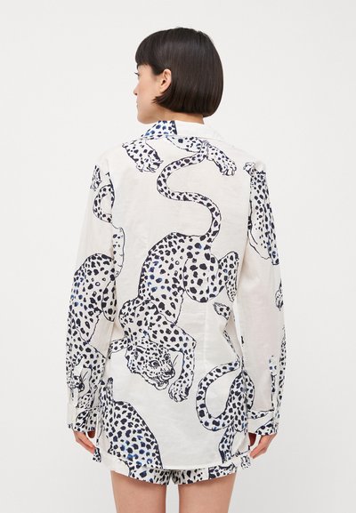 Weißes Kleidungsstück mit lockerem Schnitt, das ein blau-schwarzes Leopardenmuster zeigt. Lange Ärmel und Knopfmanschetten. Glatte Stofftextur.