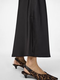 Pernas em calças largas pretas e sapatos de salto kitten com bico fino e slingback, com padrão de leopardo em castanho e preto sobre um fundo branco.
