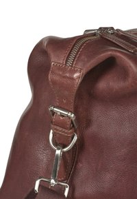 Bruine leren tas met een gestructureerde afwerking, zilverkleurige hardware, ritsafsluiting en een afneembare schouderriem met een metalen haak.