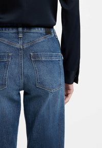 Blå denimjeans med rak skärning, utrustade med två bakfickor, förstärkta sömmar och en sydd logotypmärke på midjebandet.