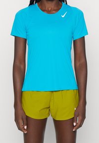 Tyrkysové sportovní tričko s kulatým výstřihem a krátkými rukávy, spárované s olivově zelenými šortkami; obsahuje bílé logo swoosh na obou kusech.