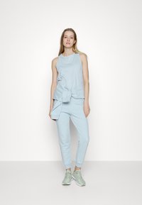 Conjunto de vestuário ativo azul claro feito de tecido macio. Top sem mangas com decote redondo e calças jogger com punhos, combinado com ténis verde claro.